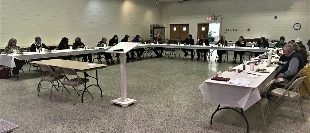 a room set up for a meeting with people seated at combined tables.