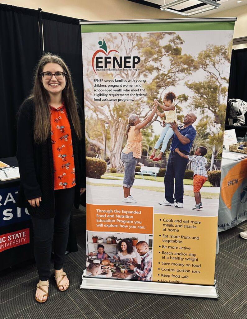 A woman stands beside an EFNEP banner.