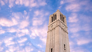 The NC State Memorial Belltower rises into a sky of puffy clouds just after sunrise. Photo by Becky Kirkland.